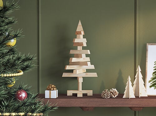 Mensola in legno con piccole decorazioni natalizie, tra cui un moderno albero in legno al centro, due alberelli più piccoli, pigne e un piccolo regalo incartato, con parte di un albero di Natale decorato visibile a sinistra.