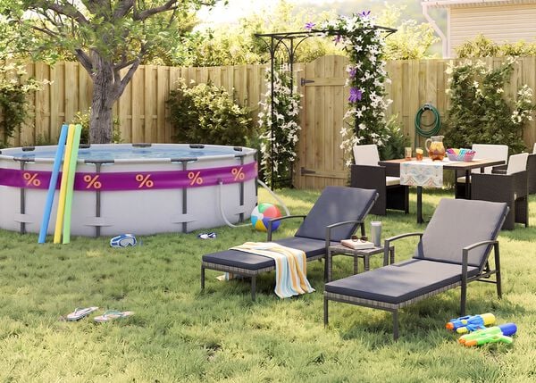 Giardino sul retro soleggiato con piscina fuori terra, tubi galleggianti, occhialini da nuoto, pallone da spiaggia e infradito sull&rsquo;erba. Due lettini prendisole in metallo nero con cuscini grigi sono sistemati accanto a un tavolino, mentre un set da pranzo da esterno con sedie scure intrecciate si trova vicino a un pergolato fiorito, una staccionata in legno e piante da giardino.