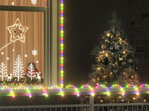 Decorazione natalizia esterna con un albero addobbato con palline dorate e luci accanto a una finestra contornata da lucine multicolori. La finestra presenta decorazioni luminose a forma di stelle, fiocchi di neve e alberi bianchi, e la ringhiera è anch’essa avvolta da luci colorate.
