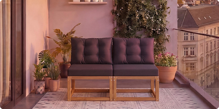 Divano modulare in legno a due posti con cuscini grigio scuro su un balcone circondato da piante in vaso e vista sulla città sullo sfondo