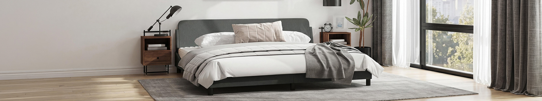 Inquadratura ampia di una camera da letto moderna con struttura letto grigio scuro, biancheria bianca e un cuscino beige con motivo a griglia. La stanza include due comodini in legno con lampade, una pianta alta in vaso e grandi finestre con tende grigie e bianche affacciate su alberi verdi.