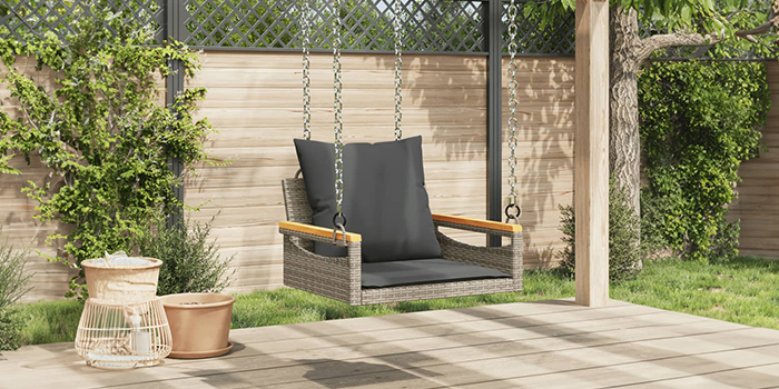 Altalena da esterno in rattan con cuscini scuri sul patio. Clicca per acquistare la collezione.