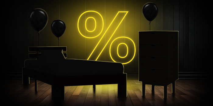  Letto nero e cassettiera con palloncini neri davanti a un cartello giallo luminoso con il simbolo della percentuale su un pavimento di legno scuro.